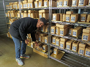 A young man puts bags of Zeke's Coffee on shelves.