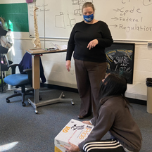 A occucational therapy instructor teaches a student how to safely lift a box.