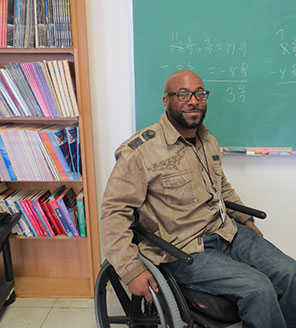 A man in a wheelchair sits in from of a classroom blackboard.