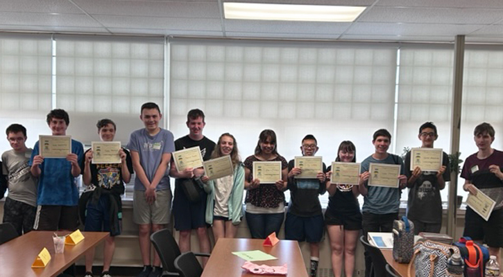 Twelve students smiling and standing holding up cerficates of completion.