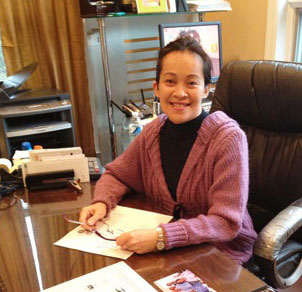 A woman sitting at a desk, holding a piece of paper and eye glasses.
