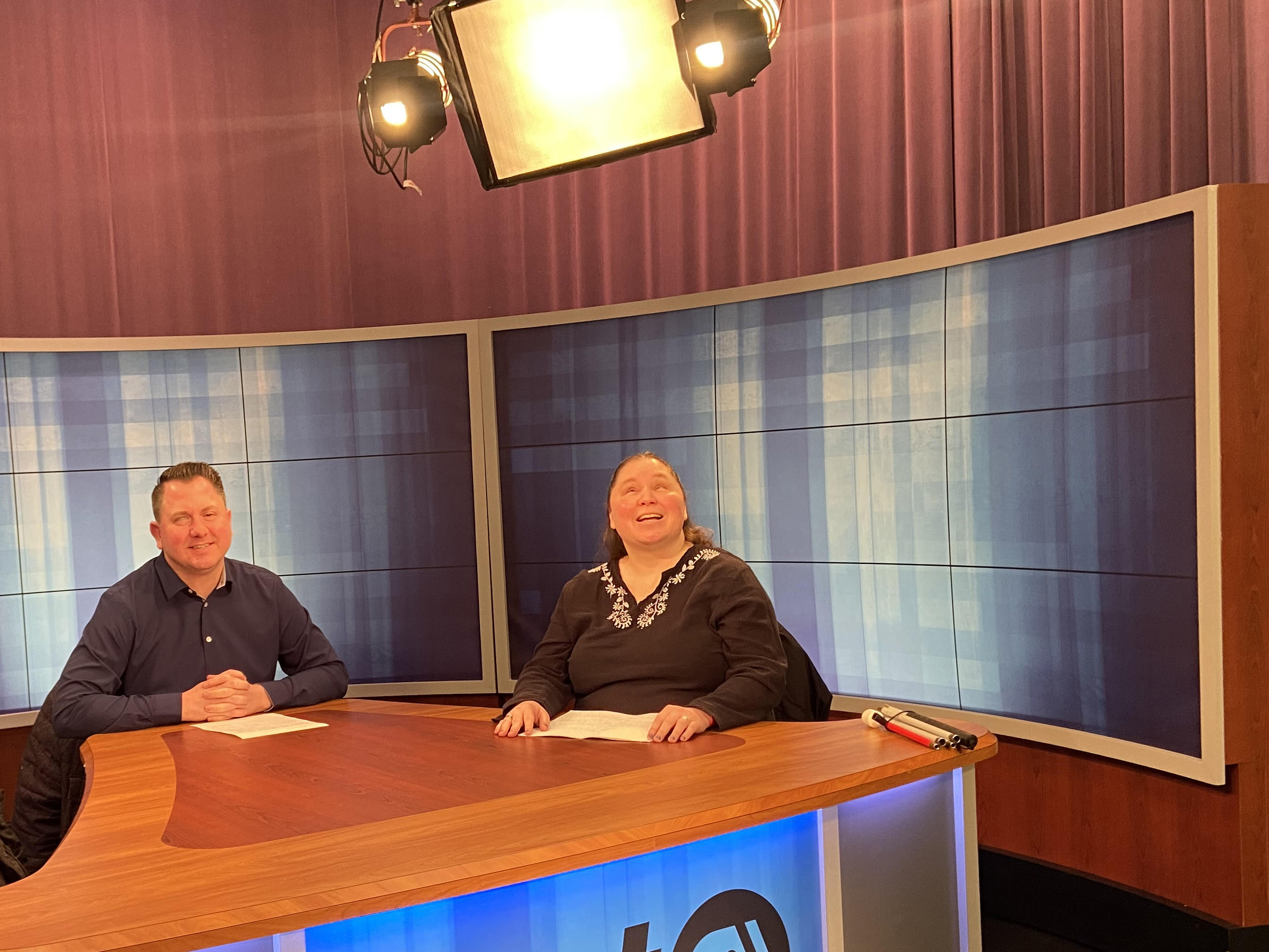 A man and a woman sitting at the television studio news desk.