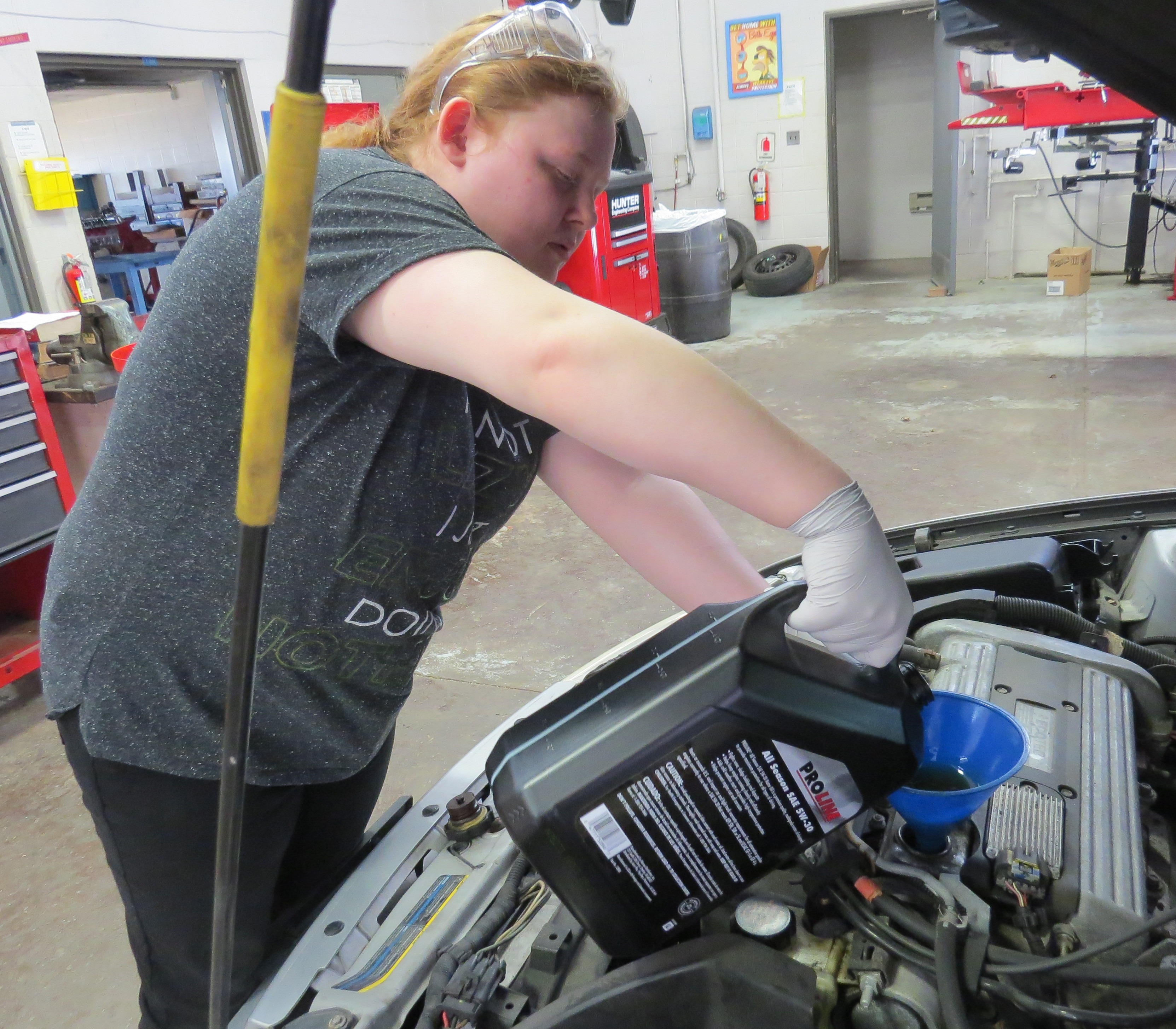 A young woman ouring oil into a car engine.