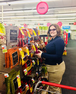 A young woman restocks a hanging display of snacks and candy in a CVS store.