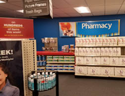 Shelves stocked with paper towels and other goods in the mock CVS store. A large sign in the back says Pharmacy.