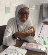 A young woman sitting at a table and holding a Krispy Kreme donut.