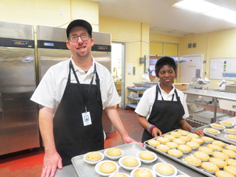 Two food services students holding trays of desserts.