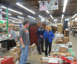 Three men and a woman in a Re-Store store. The woman is giving one of them instructions on moving some boxes.