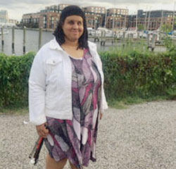 Lydia standing outside, near a waterfront, and holding a folded white cane.