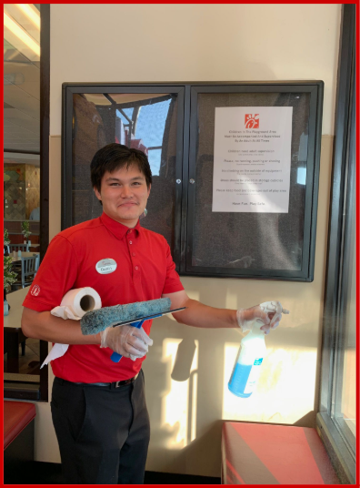 Dustin in red Chick-fil-A shirt cleaning window and holding cleaning supplies.