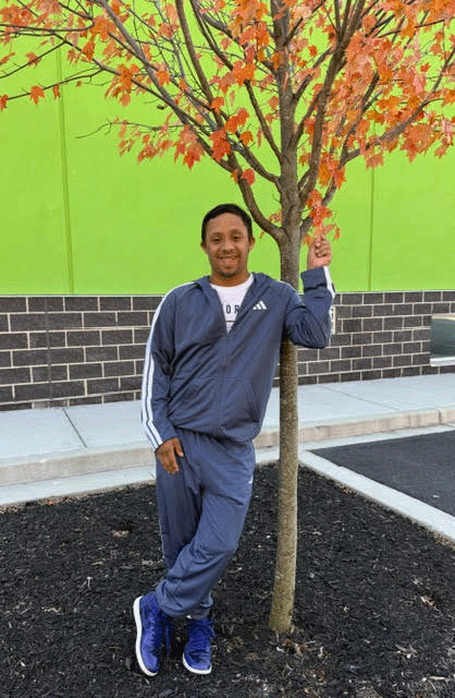 Kyrell, standing next to a small maple tree, with orange leaves.