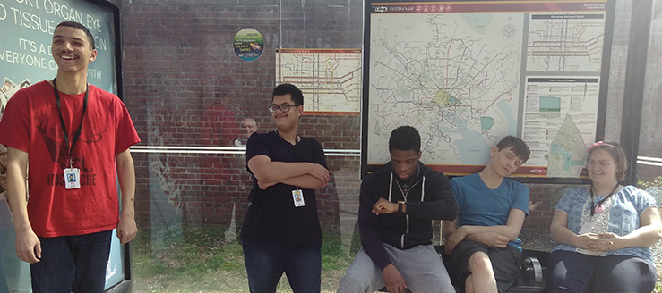 Five young adults at a bus stop. A bus route map is on the wall behind them.